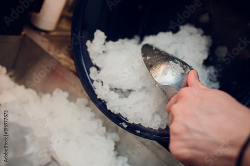 silver ice scoops in a large ice-filled bucket with blurred wine glasses in the background. Catering set-up ready for the event to begin. photo