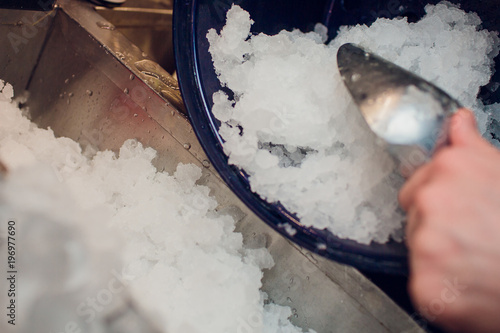 silver ice scoops in a large ice-filled bucket with blurred wine glasses in the background. Catering set-up ready for the event to begin. photo