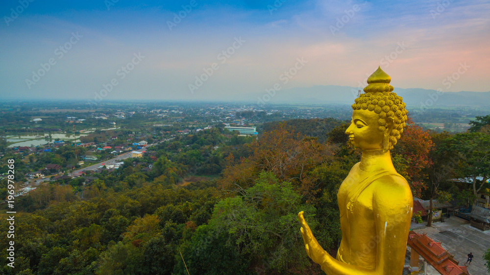 aerial photography the golden big Buddha standing statue on hilltop in sunset time at wat Phra That Jom Wae in Chiang Rai Thailand