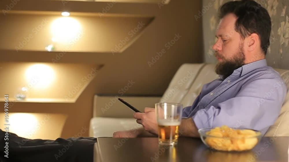 man watching a football match and pours himself a beer and eating potato chips
man watching a football match and pours himself a beer and eating potato chips