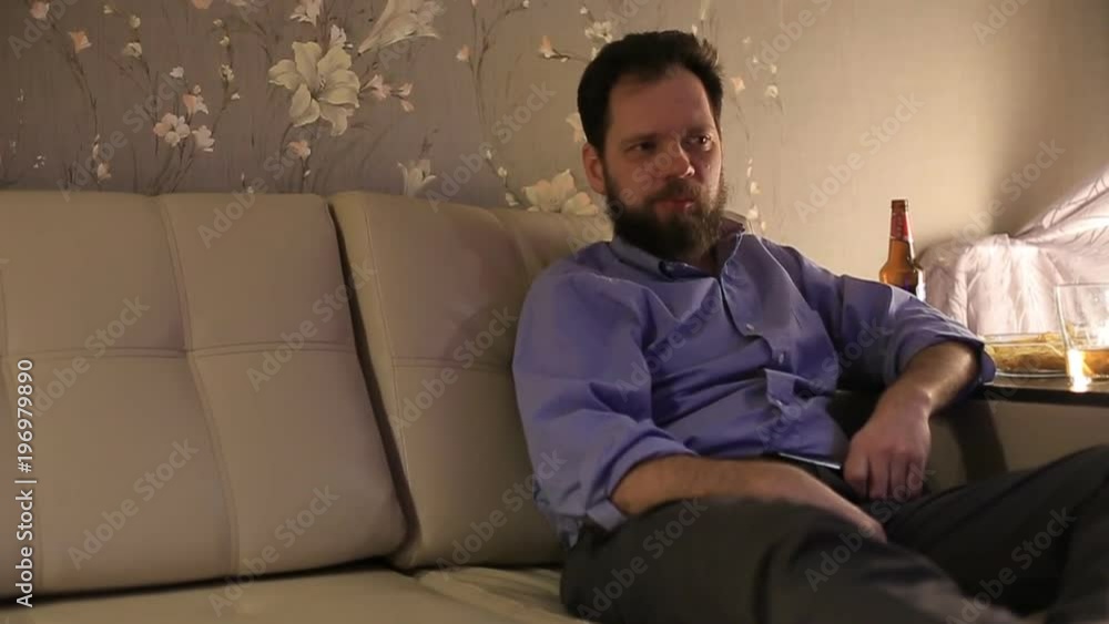 man watching a football match and pours himself a beer and eating potato chips
man watching a football match and pours himself a beer and eating potato chips