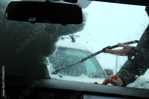 Transportation, winter, weather, people and vehicle concept - man cleaning snow from car with scraper. scrubber in man's hand. Shooting from inside the car interior. Twilight. Cleaning the car wipers