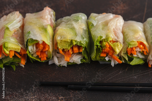 Fresh handmade vegan asian spring rolls with rice noodles, avocado, carrots and tahini dressing on dark background, copy space.