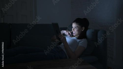 lateral pan shot of young beautiful happy and relaxed latin woman lying on home couch late night using digital device laptop tablet pad watching internet movie 