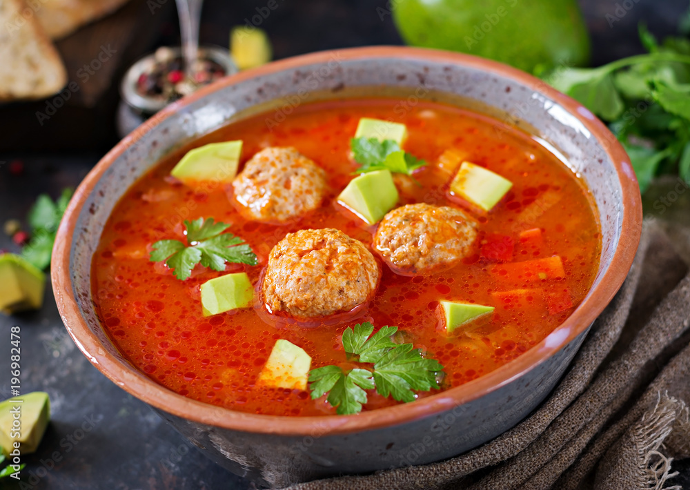 Spicy tomato soup with meatballs and vegetables. Served with avocado and parsley. Healthy dinner