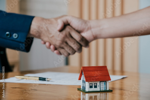 Estate agent shaking hands with his customer after contract signature, Contract document and house model on wooden desk photo