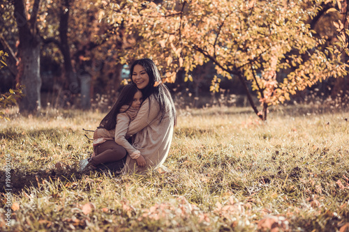 Beautiful young woman and her little kid relaxing in autumn garden.