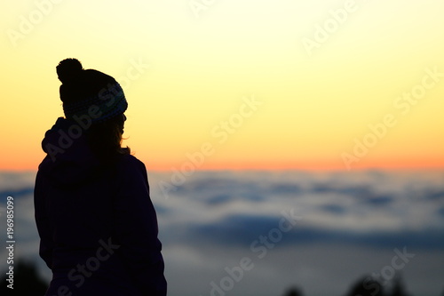 Woman hiker over a sea of clouds in the sunset