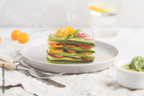 Raw vegan zucchini lasagna with vegetables and pesto sauce, light background. Vegetarian raw diet concept, copy space.