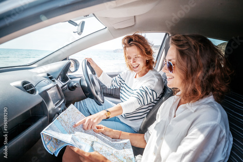 Two attractive friendly young women enjoying a day trip to town viewed through the open window of their car grinning happily at the camera photo