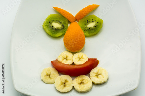 Horizontal View of Close Up some Pieces of Fruit Forming a Face Expression with Banana, Kiwi, Orange and Tomato on White Background