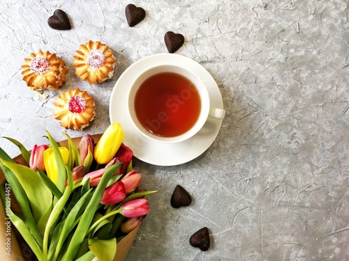 multi-colored tulips with a Cup of tea with cakes and chocolates