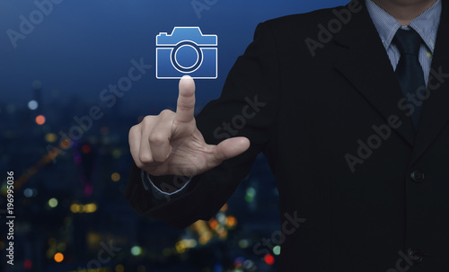 Businessman pressing camera flat icon over blur colorful night light city tower, Business camera service concept