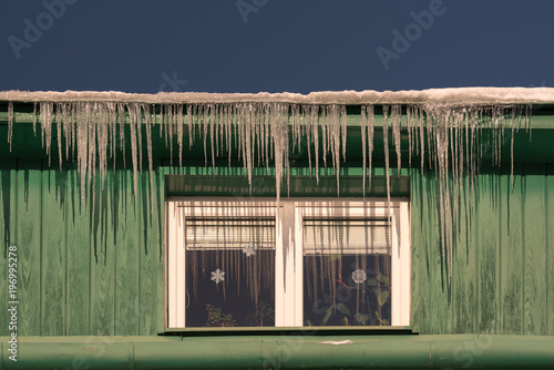 Green old house with winter frozen crystals in front of the windows