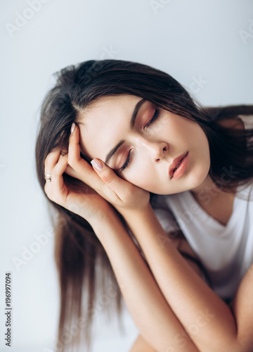 Beautiful young woman with closed eyes touching her face