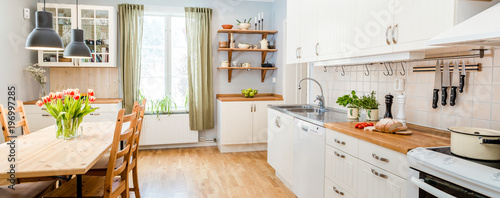 banner of a kitchen with kitchen table  and breakfast at the kitchen counter top white cupboards and wooden floor photo