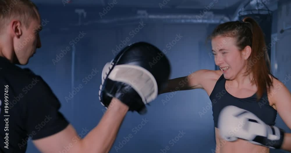 Athletic woman trains her punches on a punching bag that her partner Athletic woman trains her punches on a punching bag that her partner