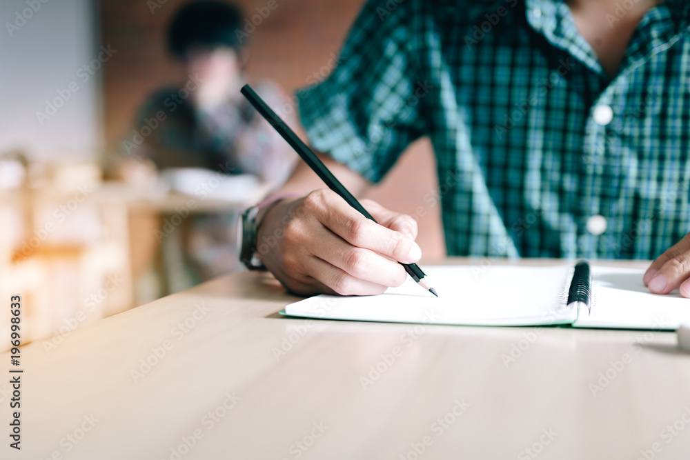 Close up of student hand writing on paper with a pencil in classroom. Close up of student hand writing on paper with a pencil in classroom.