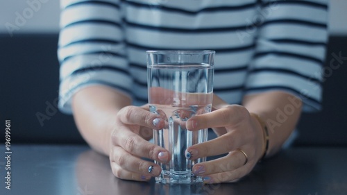 closeup of woman's hand with glass of water touching it