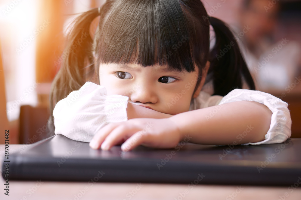 Asian children cute or kid girl upset or angry and sad feel with touchy on book and wood table with sunlight from window side at home on vintage style and soft focus Asian children cute or kid girl upset or angry and sad feel with touchy on book and wood table with sunlight from window side at home on vintage style and soft focus