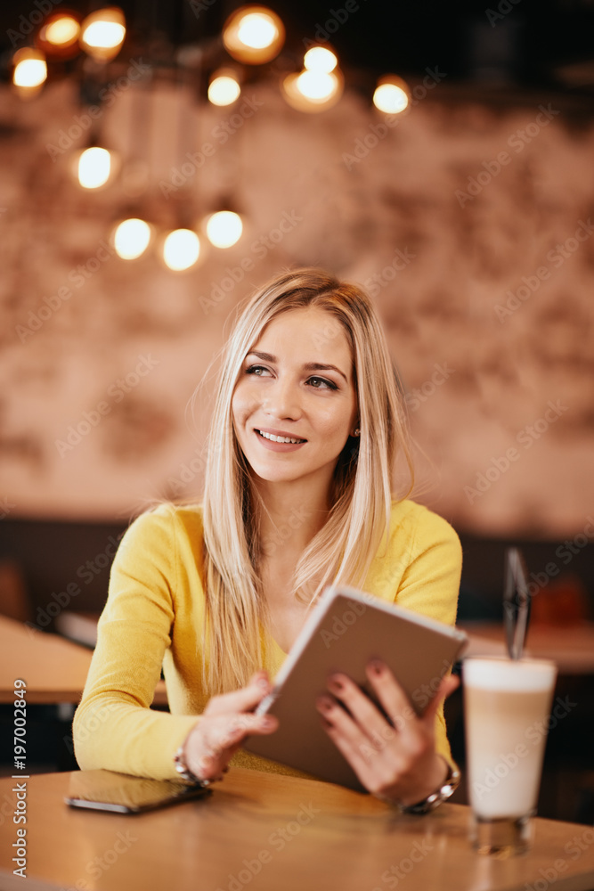 Young caucasian woman using tablet while sitting in cafe and drinking coffee. Young caucasian woman using tablet while sitting in cafe and drinking coffee.