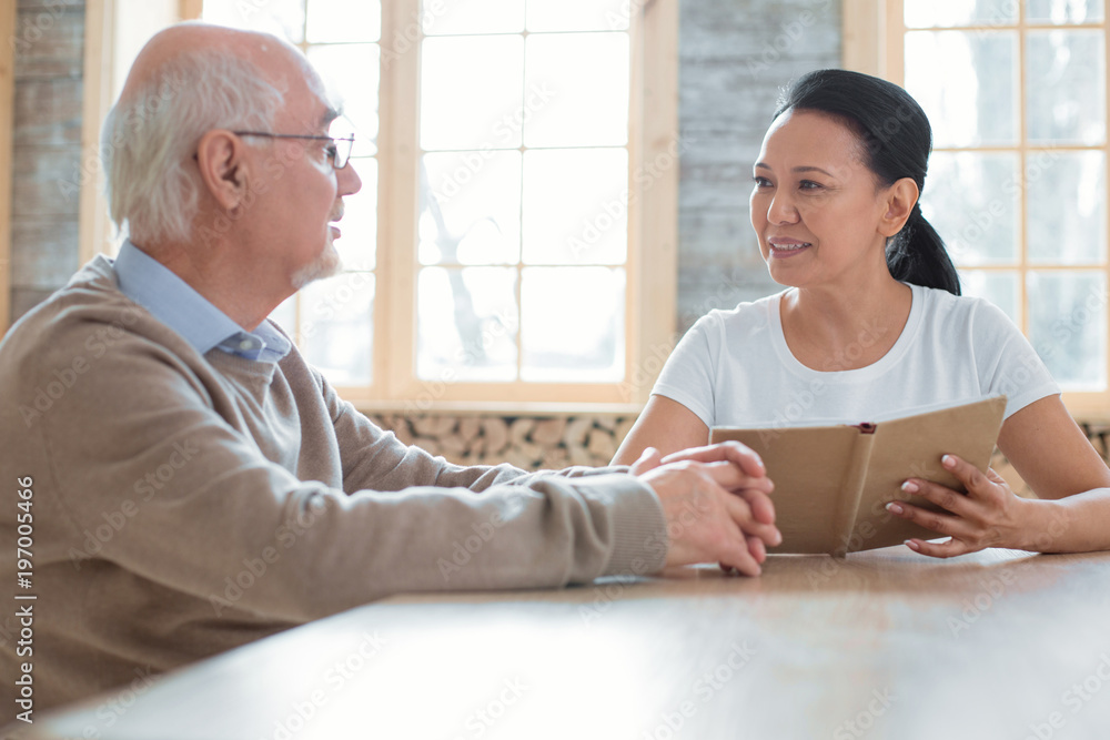 Help people. Beautiful happy volunteer holding book while talking to senior man and looking at him Help people. Beautiful happy volunteer holding book while talking to senior man and looking at him