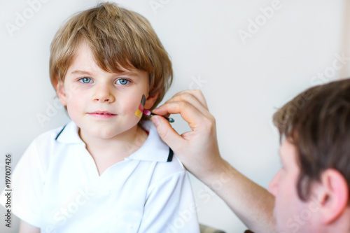 Young dad painting flag on face of little son for football or soccer game.
