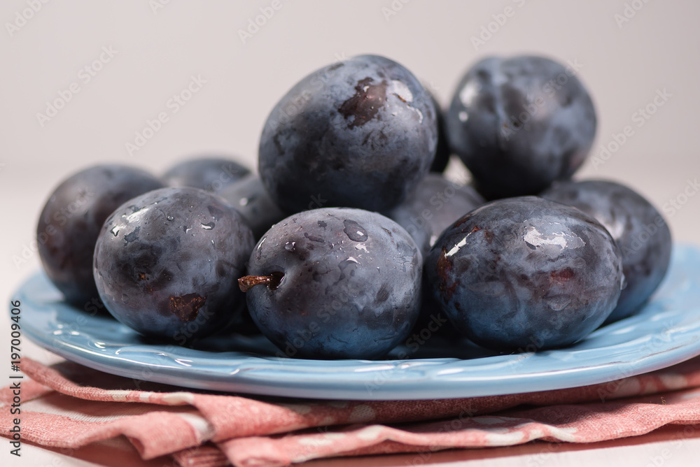 Fresh ripe blue plums on plate, wooden table with napkin Fresh ripe blue plums on plate, wooden table with napkin