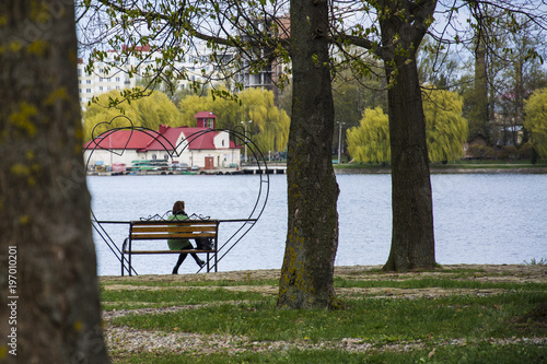 Lonely woman sitting alone on a bench in a pack near the lake