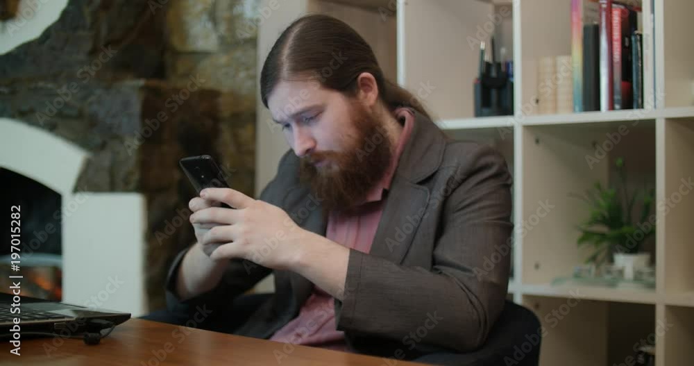 Bearded informal man uses a smartphone in office Bearded informal man uses a smartphone in office