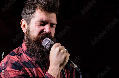 Man with tense face holds microphone, singing song, black background.