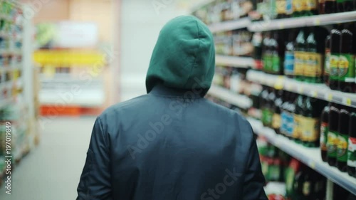 Portrait man steals bottle of alcohol in supermarket go away shot behind shoplifting larceny technology crime store theft criminal customer illegal retail poor looting lifting security shop consumer photo