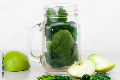 Green smoothie in glass jar with fresh organic green vegetables and fruits on grey background. Spring diet, healthy raw vegetarian, vegan concept, detox breakfast, alkaline clean eating. Copy space