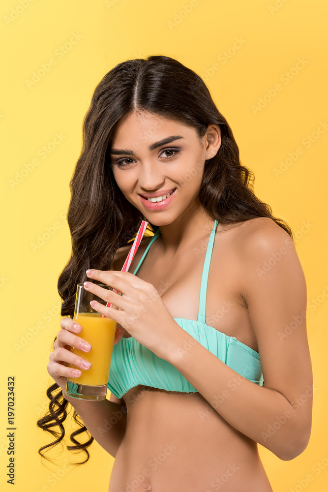 beautiful smiling girl posing in bikini with glass of juice, isolated on yellow