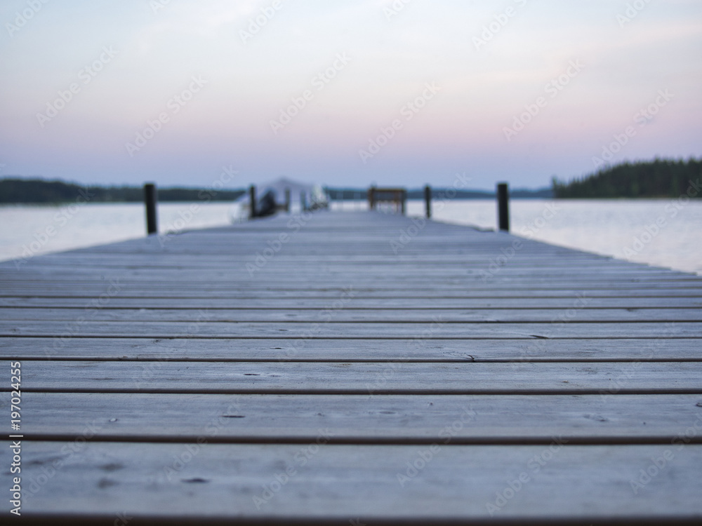 A closeup of a dock and a finnish lake scenery during summer. A boat at the background