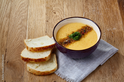 Ceramic bowl of pumpkin soup on napkin over rustic wooden background, close-up, selective focus, top view.