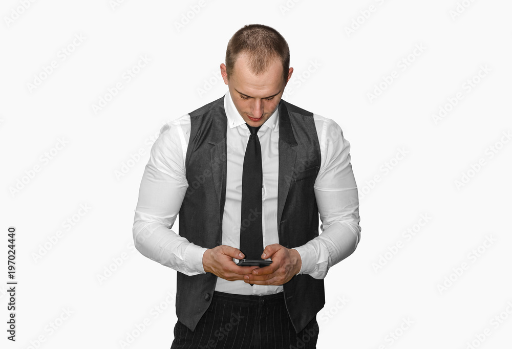 young man in a vest uses a mobile phone, typing sms on gray background