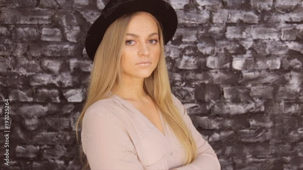 A girl in a black hat and a gray shirt posing against a brick wall background A girl in a black hat and a gray shirt posing against a brick wall background
