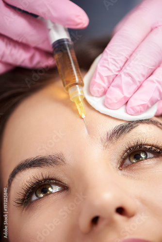 Macro photography woman with beautiful eyes gets injection for female forehead face. Plastic aesthetic facial surgery in beauty clinic.