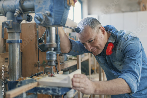 Mature carpenter using drill press in workshop