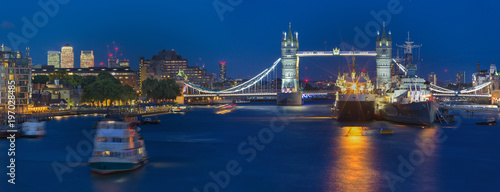 London - The panorama of Tower bridge with the ships and Canary Wharf in the background at dusk.