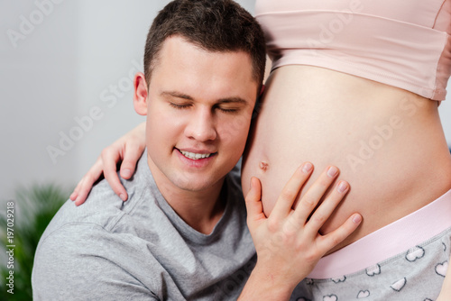 cropped shot of happy man listening to the belly of pregnant woman