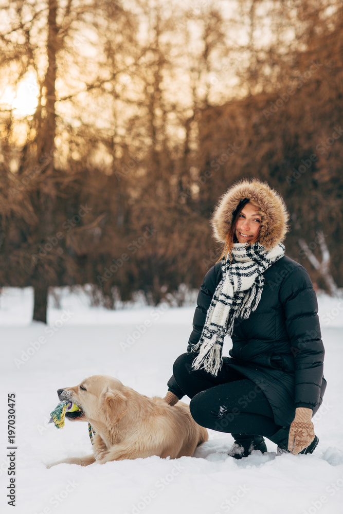 Photo of smiling girl with labrador on background of trees in winter park