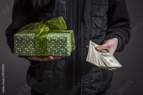 The guy is holding a box with a gift in one hand and money in another