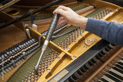 closeup of hand and tools of tuner working on grand piano photo