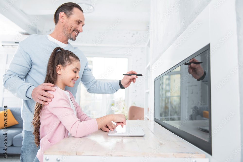 Obraz premium Age of technology. Nice pleasant delighted father and daughter standing together and using modern technologies while being in a good mood