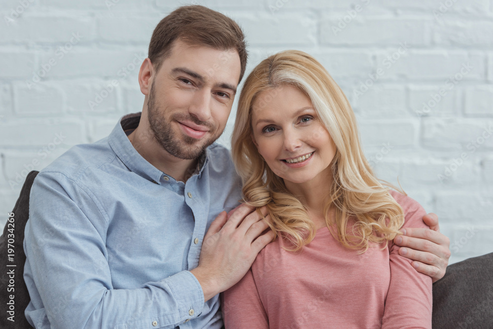 portrait of smiling son hugging mother while resting on sofa at home