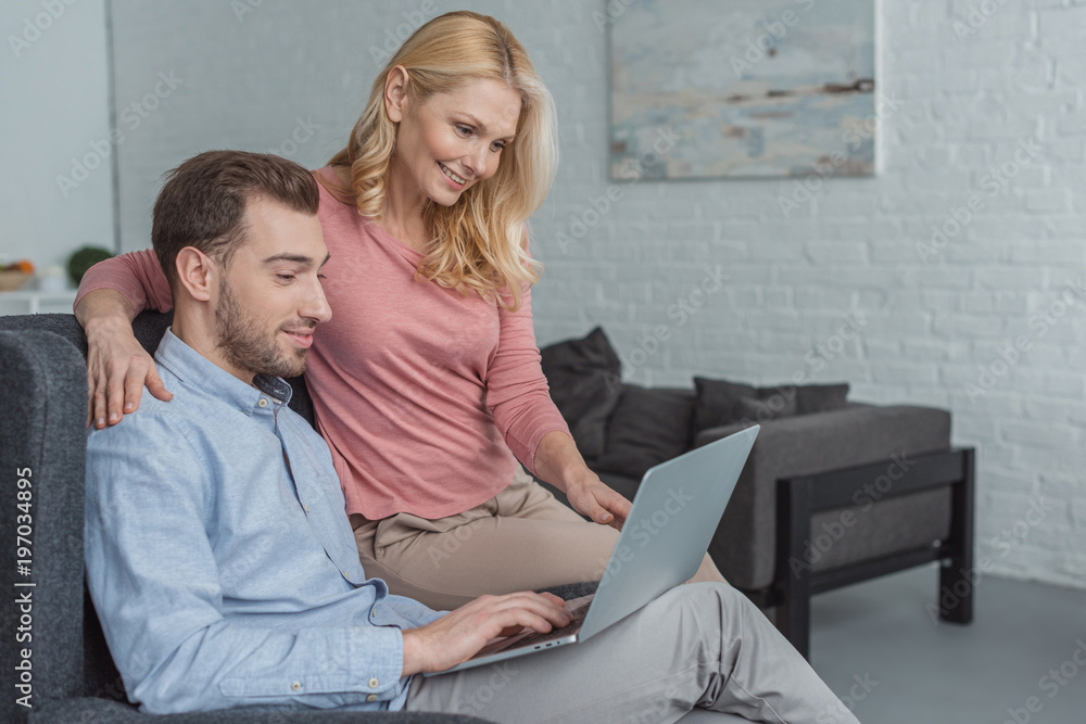 side view of mother and grown son using laptop together at home side view of mother and grown son using laptop together at home