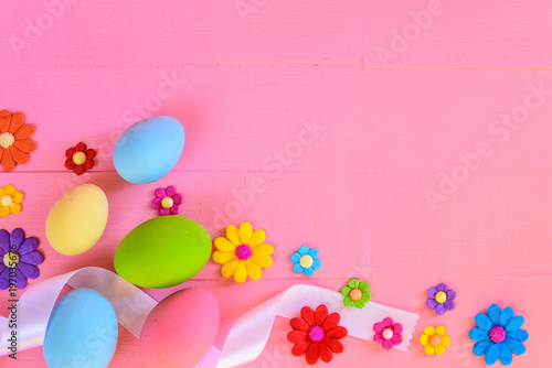 Easter eggs with colorful paper flowers on bright pink wooden background.