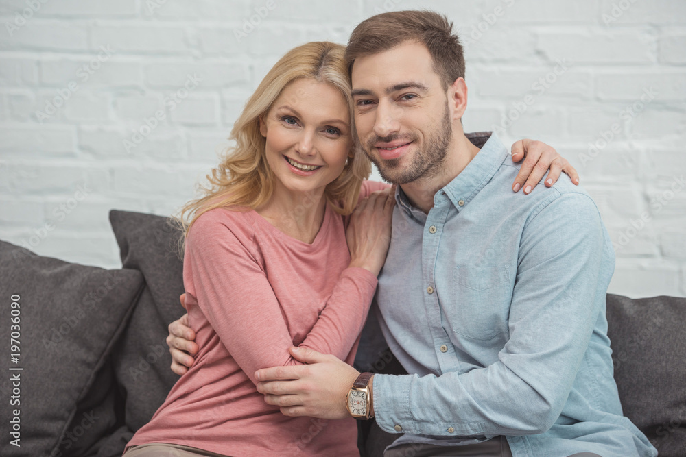 portrait of smiling mother and grown son hugging each other while sitting on sofa portrait of smiling mother and grown son hugging each other while sitting on sofa